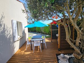 Una terraza de madera con una mesa y sillas, un paraguas azul y una pérgola de madera adornada con flores.