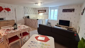 A compact living space with a dining area, a sofa, a TV, and a kitchen in the background. - Charming cottage with parking - 2 guests in village center (Choloy-Ménillot)