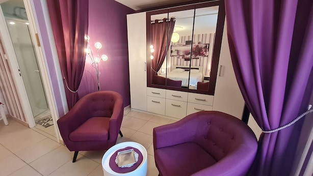 A room with purple curtains, a bed with a white headboard, a wardrobe with a mirror, and two purple armchairs. - Charming cottage with parking - 2 guests in village center (Choloy-Ménillot)