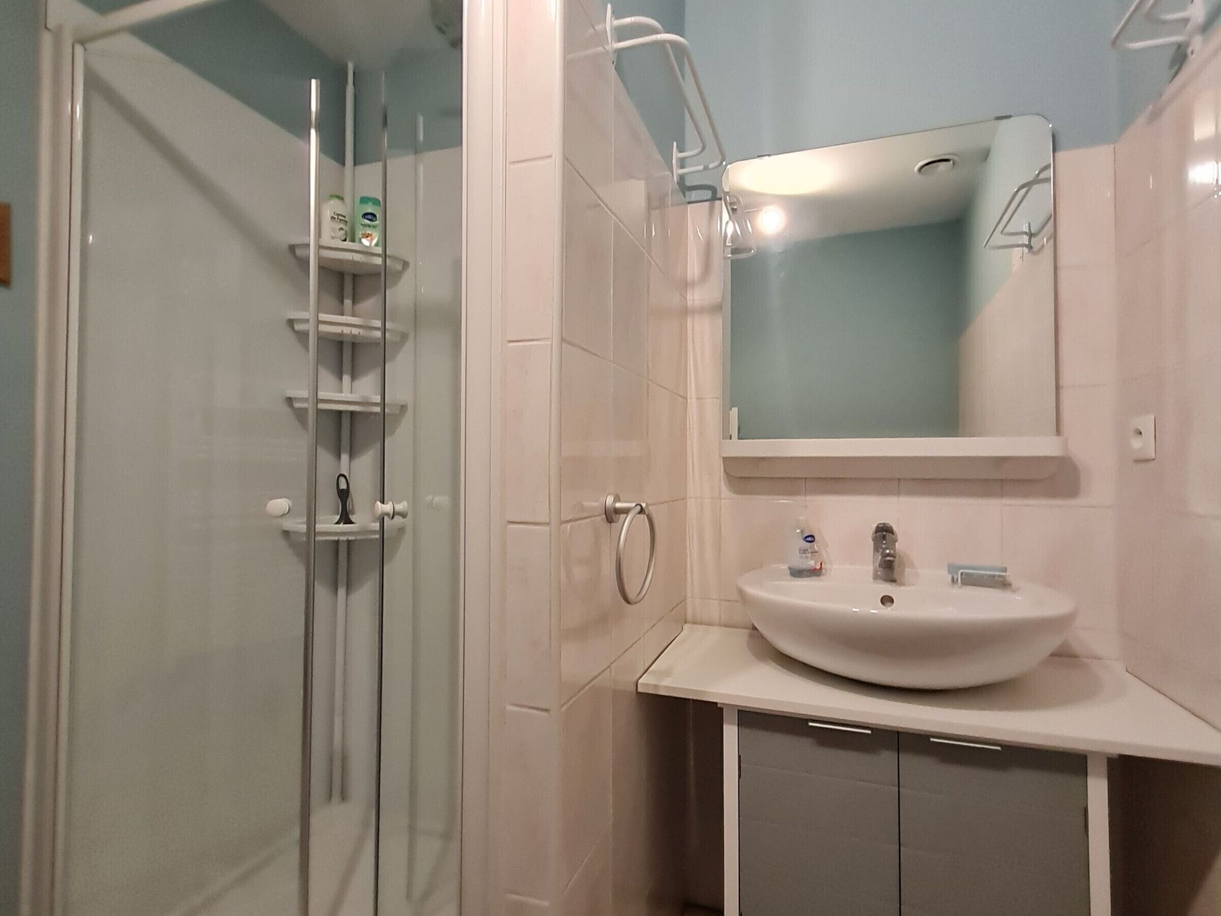 Een badkamer met een douchecabine van glas, een wit wastafelmeubel met een spiegel erboven en een betegelde muur.