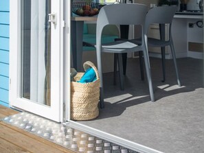 Una habitación con puerta corredera de vidrio, una cesta trenzada con un objeto azul y dos sillas grises.