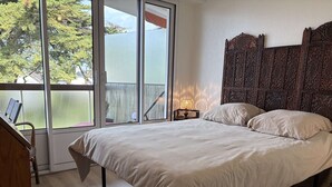 Quarto com uma cama grande, mesa de cabeceira, abajur e vista para o exterior através de uma porta de vidro.