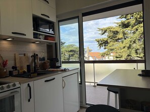 Une cuisine avec des meubles blancs, un four à micro-ondes et une vue sur les arbres et les bâtiments à l’extérieur.