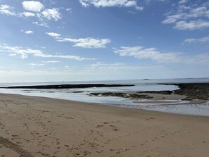 Une plage parsemée d'empreintes, un ciel dégagé et une terre lointaine à l'horizon.