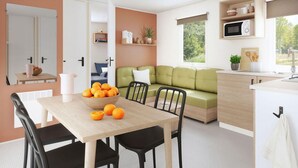 A modern kitchen with a dining area, a green sofa, and a bowl of oranges on the table. - Mobile home AC - 6 guests (Valloire-sur-Cisse)