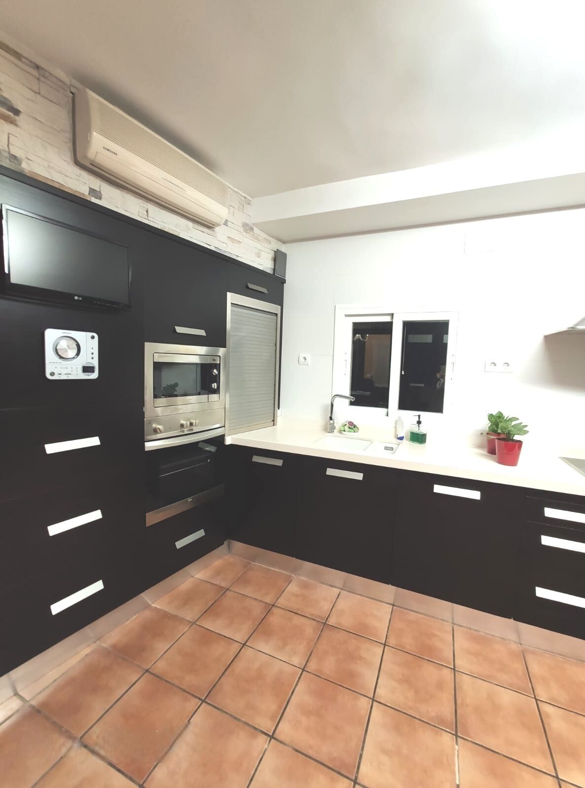 Een keuken met een inbouwoven, magnetron en een groot raam.