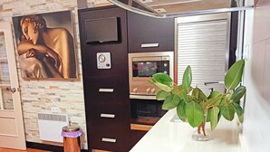 Cocina compacta con horno empotrado, microondas y estufa. Hay un cubo de basura pequeño y una planta en maceta en la encimera.