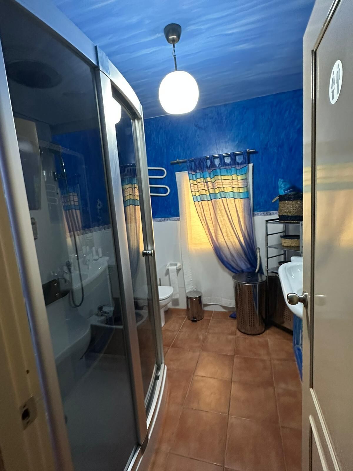 Une salle de bain avec une douche à parois de verre, des toilettes, un lavabo et un luminaire au plafond.