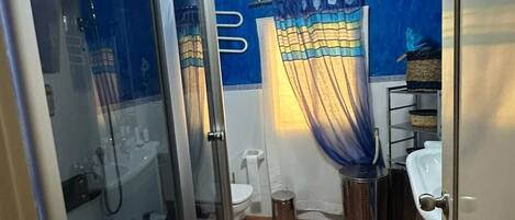 Une salle de bain avec une douche à parois de verre, des toilettes, un lavabo et un luminaire au plafond.