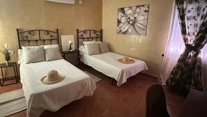 Una habitación con dos camas, ventilador de techo, aire acondicionado, un cuadro en la pared y una ventana con cortinas.