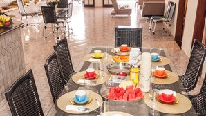 Un comedor con mesa de vidrio, sillas negras y piso de baldosas.