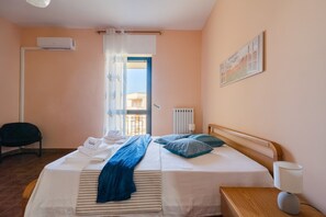 A hotel room with a bed, a chair, a radiator, and a window with curtains. - Holiday Home 'Casa Elena in Otranto' with Balcony, Wi-Fi and Air Conditioning (Otranto)