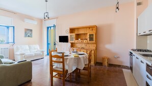 Ein Wohnzimmer mit einer Couch, einem Esstisch gedeckt mit Tellern und Gläsern, einer Küchenzeile mit Schränken und einem Fernseher.