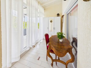 Un coin repas avec une table en bois, une chaise rouge, des rideaux blancs et une plante en pot.