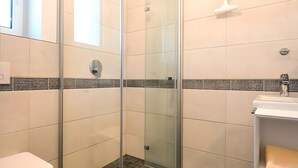 Ett modernt badrum med en dusch som är avskärmad med glasväggar, en toalett och ett handfat.