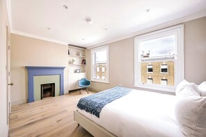 Een slaapkamer met een bed, een blauwe stoel, een open haard en uitzicht op een gebouw van baksteen.
