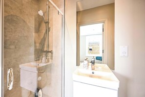 Een badkamer met een douchecabine van glas, een witte wastafel en een spiegel die een kamer met een raam weerspiegelt.