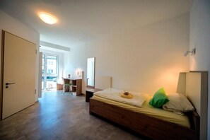 Un dormitorio con cama, escritorio y silla. Hay una puerta que conduce a otra habitación.