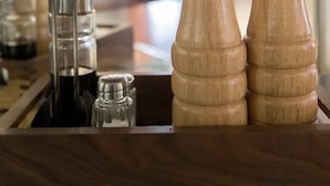 Una barra de madera con saleros y pimenteros, un recipiente de vidrio y un gancho metálico.