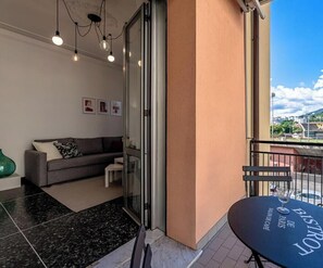 Een balkon met een tafel, een bank en een glazen deur die naar een kamer leidt.