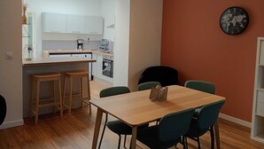 A modern kitchen with white cabinets, a dining area with a wooden table and green chairs, and a world map clock on the wall.