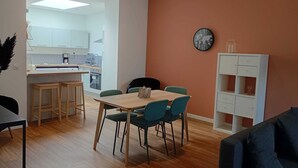 A modern living room with a dining area, a kitchen in the background, and a clock on the wall.