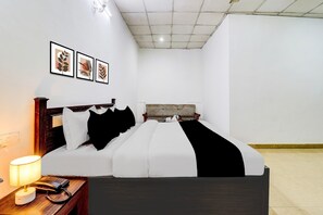 A hotel room with a bed, bedside table, lamp, and framed artwork on the wall. - Deluxe Bhagwan Guest House (Dehradun)