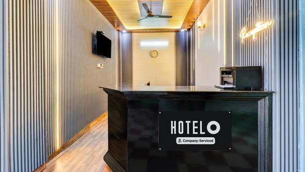 A hotel reception area with a black reception desk, a clock on the wall, and a neon sign. - Deluxe Bhagwan Guest House (Dehradun)