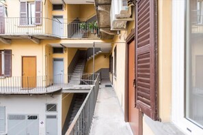 A narrow corridor with a staircase leading to an upper floor, a closed shutter door, and a balcony with railings. - The apartment, a two-room apartment of 36 sqm, is located on the 1st floor of a traditional building with a terrace, NOT equipped with a lift, recently renovated and with a modern design. The area is lively and very well connected to both the city center (Milan)