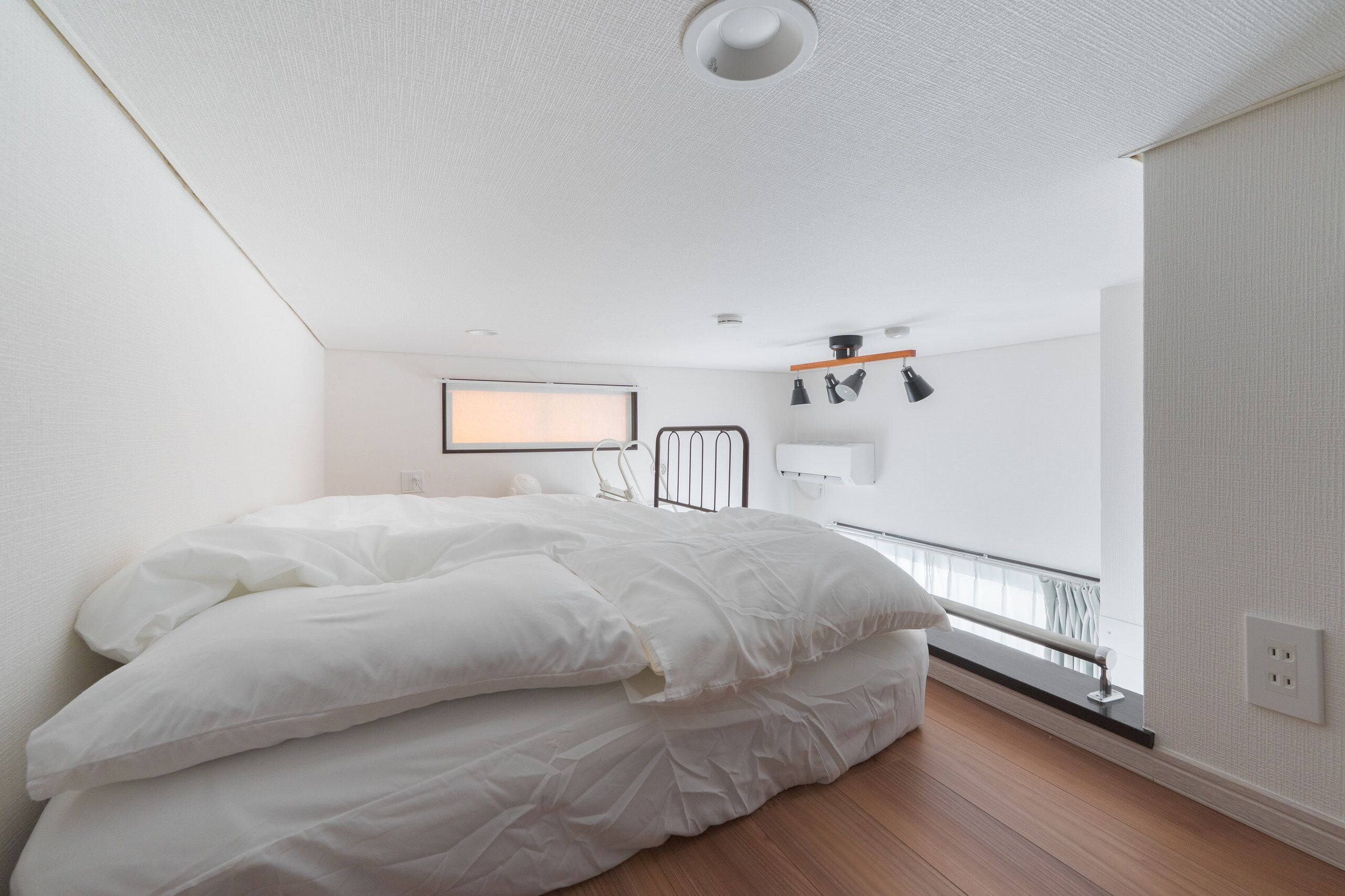 A bedroom with a bed, a window, a wall-mounted heater, and a ceiling light.
