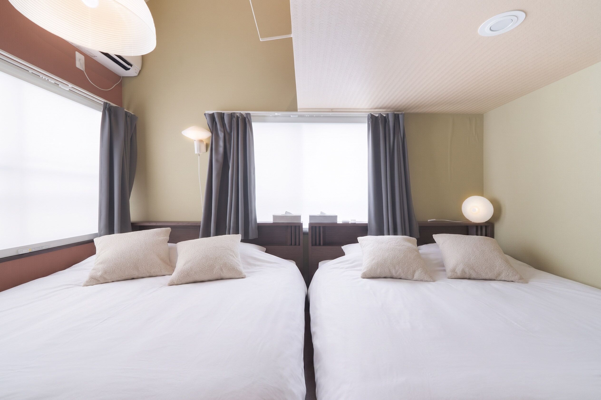 Habitaci ón de hotel con dos camas, un ventanal con cortinas, una lámpara de techo y un aire acondicionado instalado en la pared.