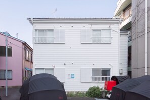 Un edificio de dos pisos con revestimiento blanco, varias ventanas con contraventanas y un pequeño balcón.