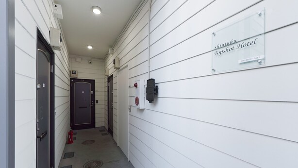 A hallway with a sign for 'Shinjuku Topshot Hotel' and a fire alarm on the wall.