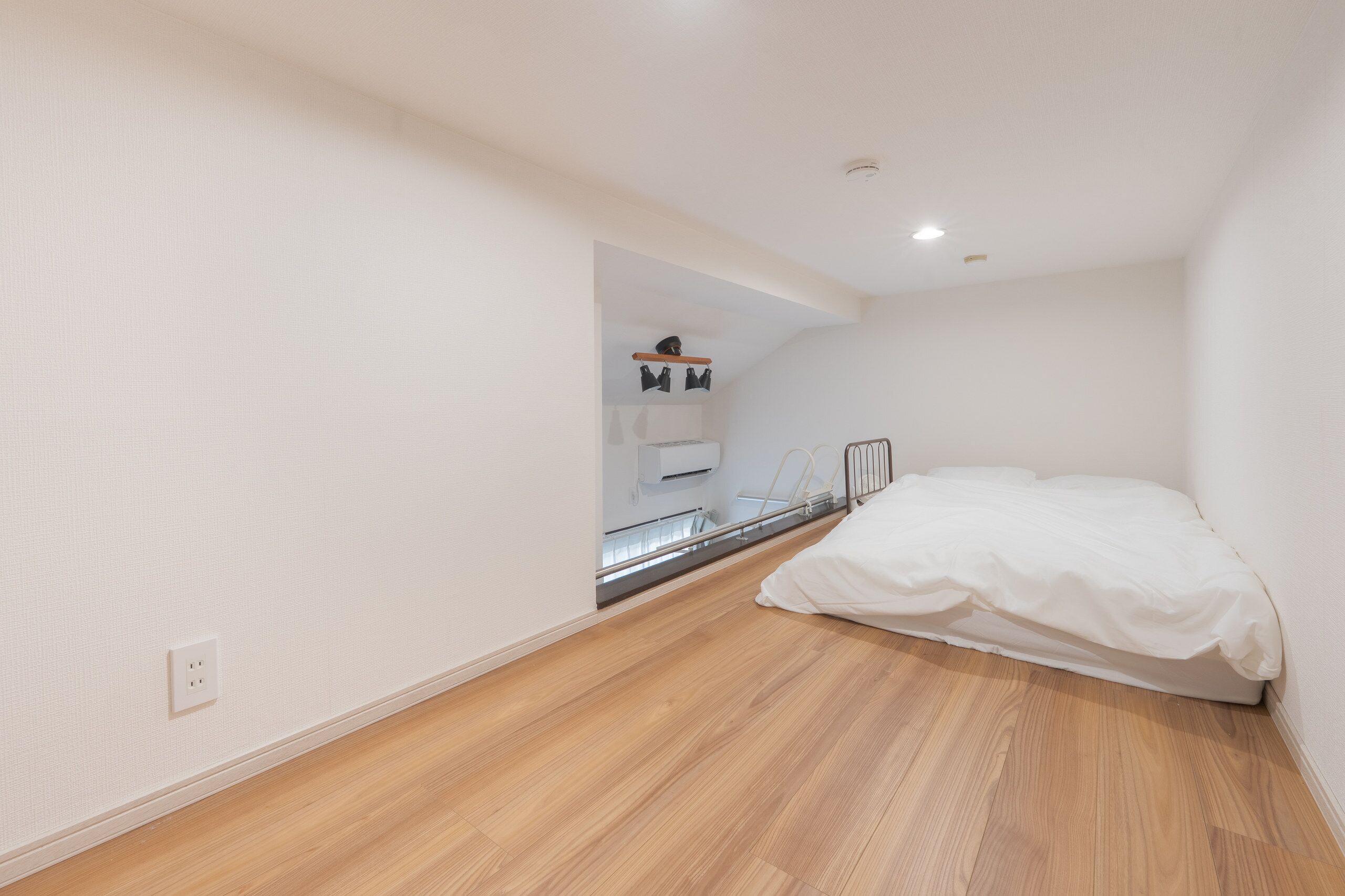 Ein Schlafzimmer mit Holzboden, einem Bett, einer kleinen Küchenzeile und einer weißen Wand.