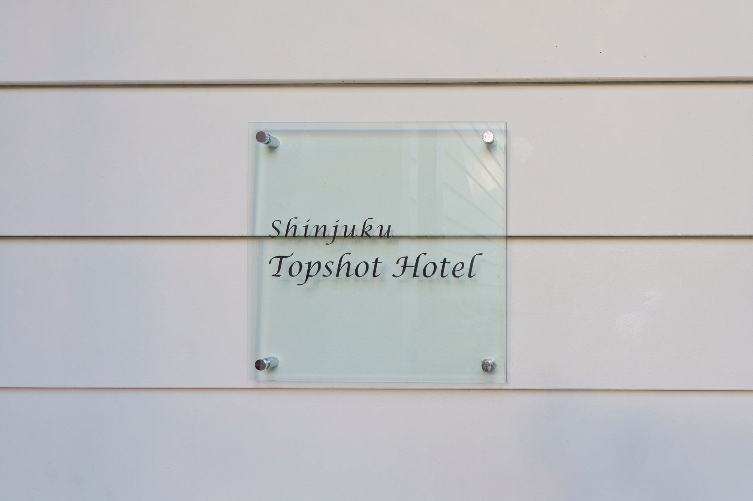 Een glazen bord met de naam 'Shinjuku Topshot Hotel' bevestigd aan een muur.