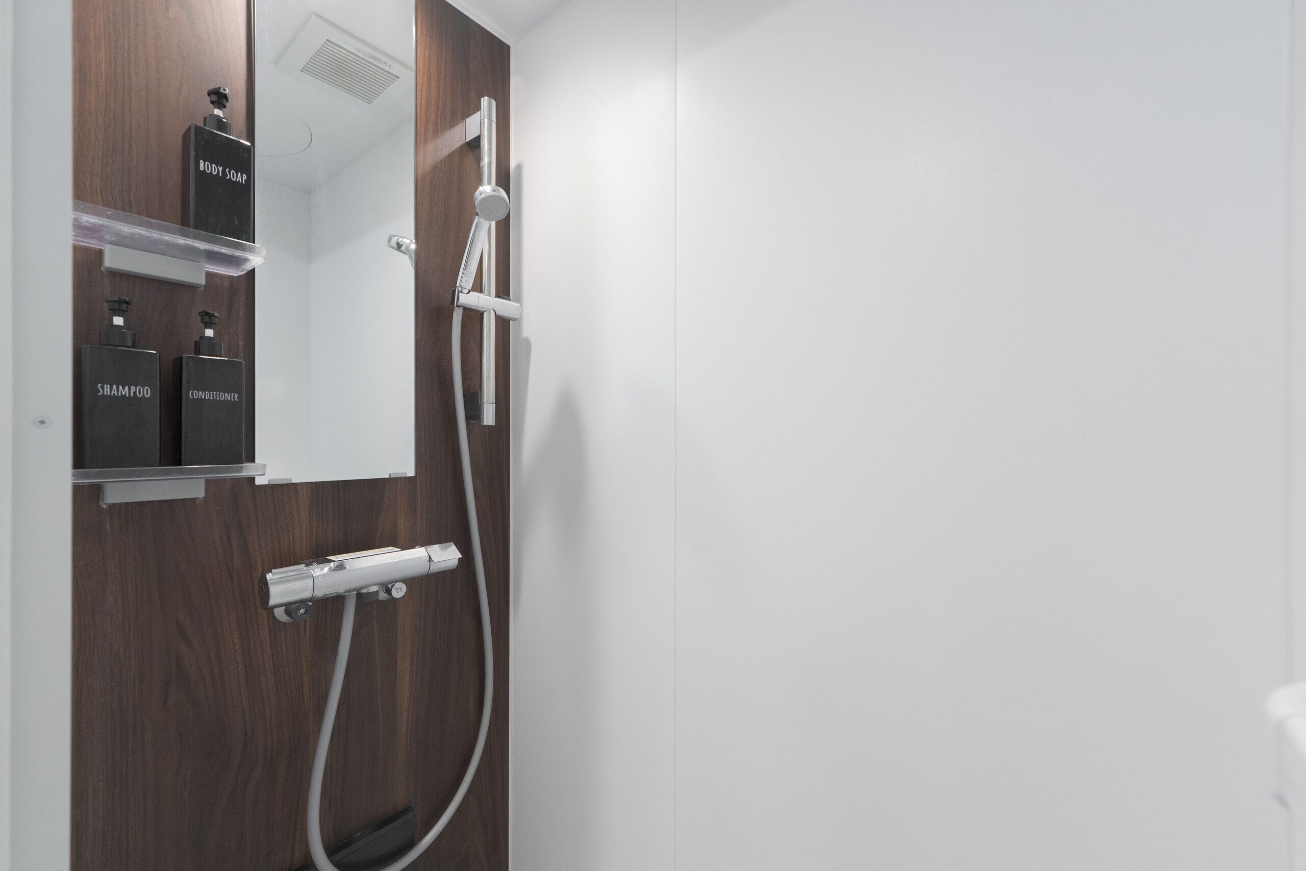 A modern bathroom with a wooden vanity, a mirror, and a shower with a handheld showerhead.