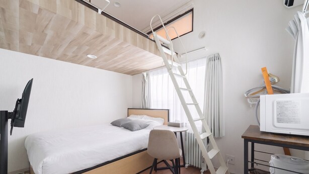 Une chambre d’hôtel compacte comprenant un lit superposé, un bureau avec une chaise, une télévision et un four à micro-ondes.