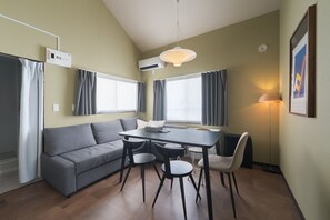Una sala moderna con un sofá gris, una mesa de comedor con sillas, una lámpara colgante y un radiador.