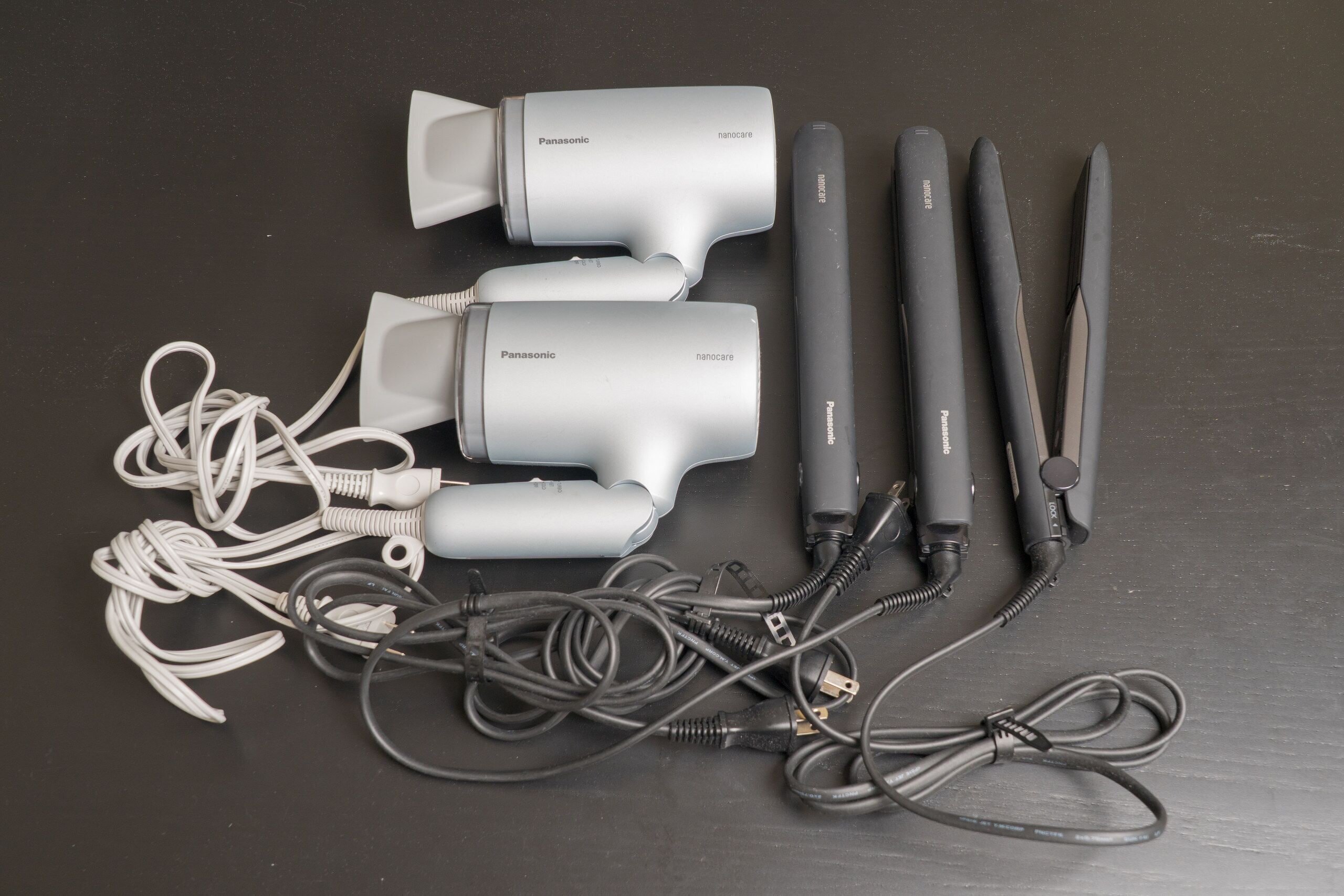 A set of Panasonic hair styling tools with cords and attachments laid out on a dark surface.