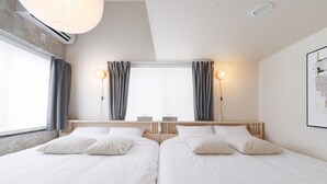 A hotel room with two beds, a window with curtains, a wall-mounted light fixture, and a ceiling vent.