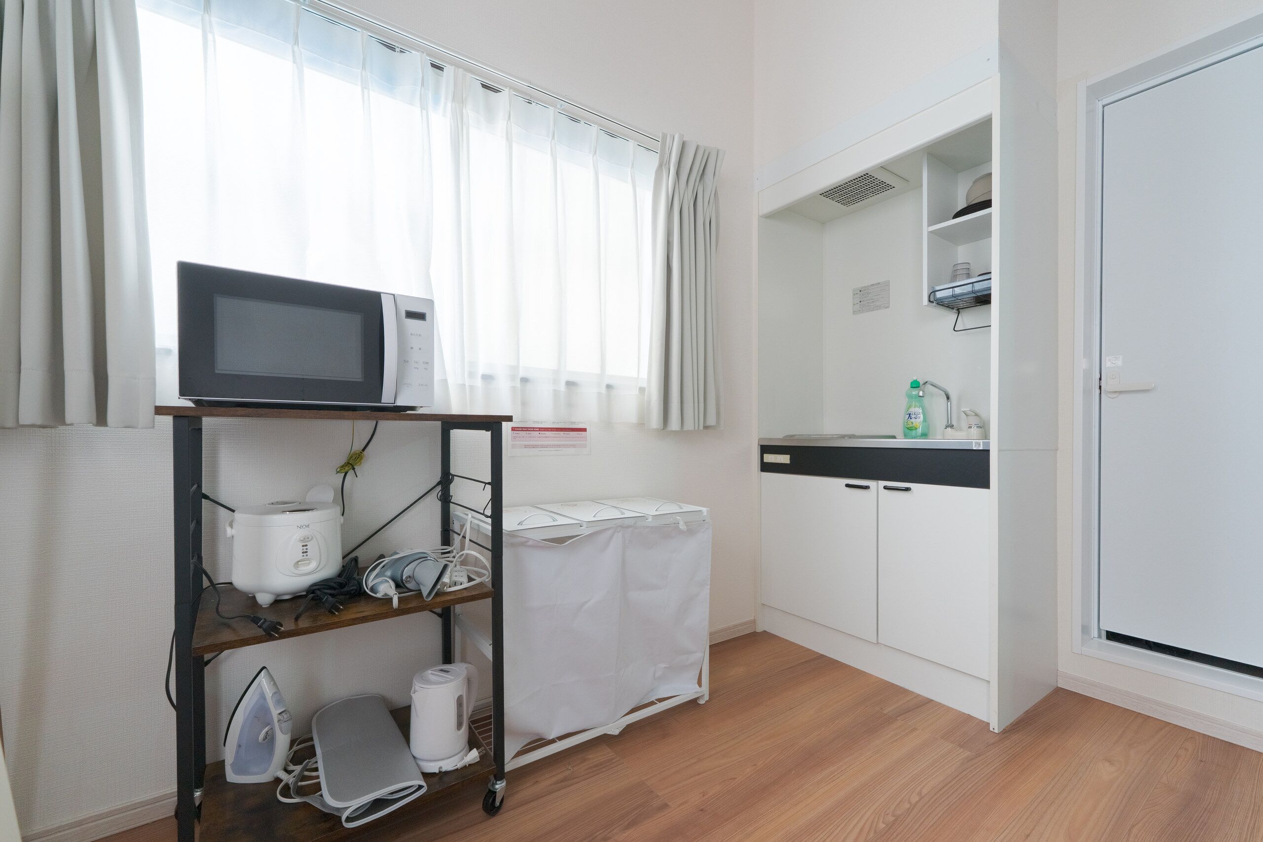 A compact kitchen with a microwave, a kettle, and a small ironing board.