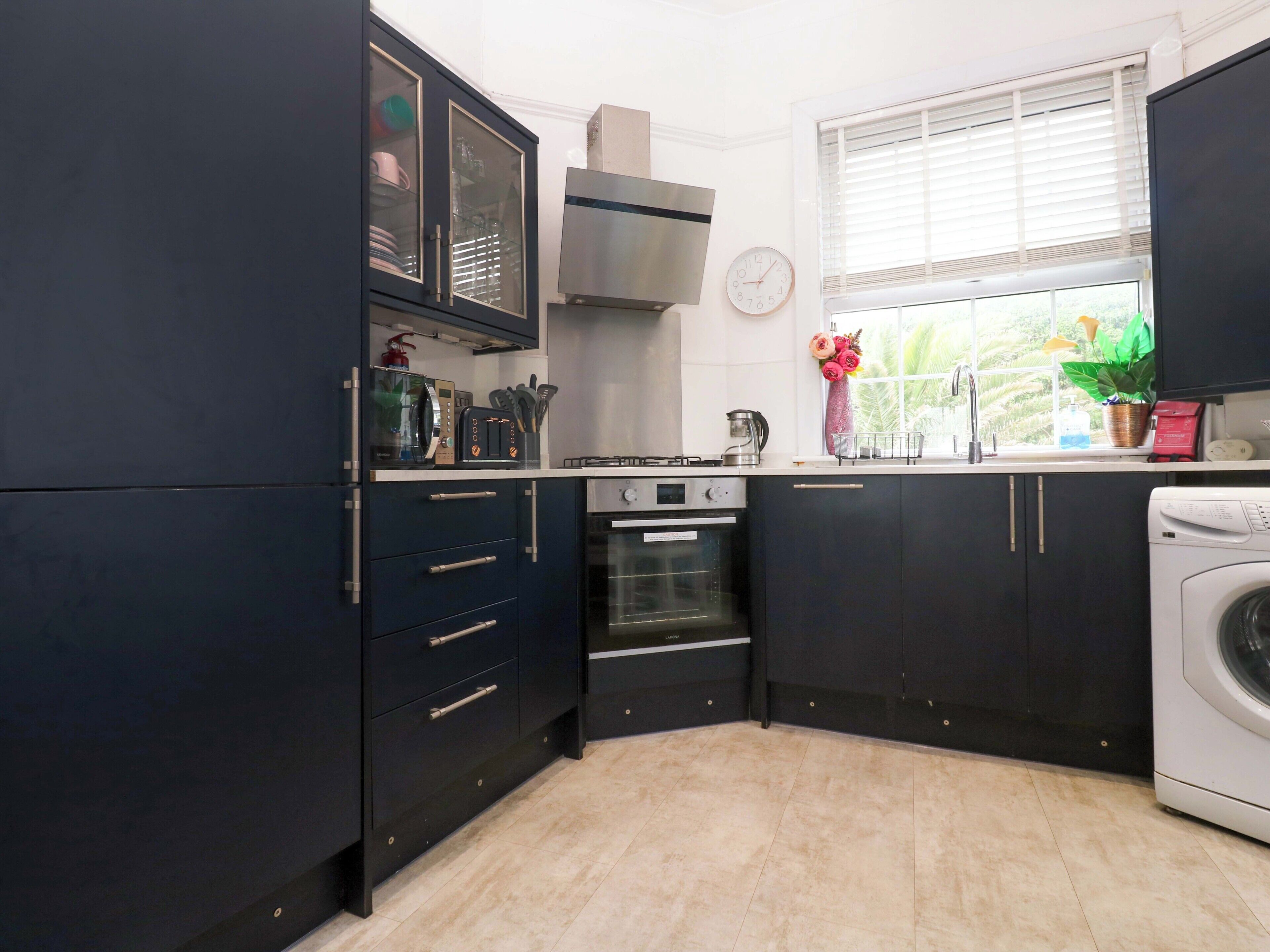 Cocina compacta con armarios oscuros, horno empotrado, microondas y lavadora.