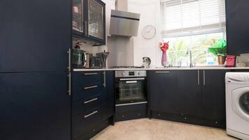 Cocina compacta con armarios oscuros, horno empotrado, microondas y lavadora.