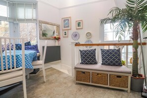 Una habitación con una cuna, un banco con cestas, una planta en maceta y relojes de pared.
