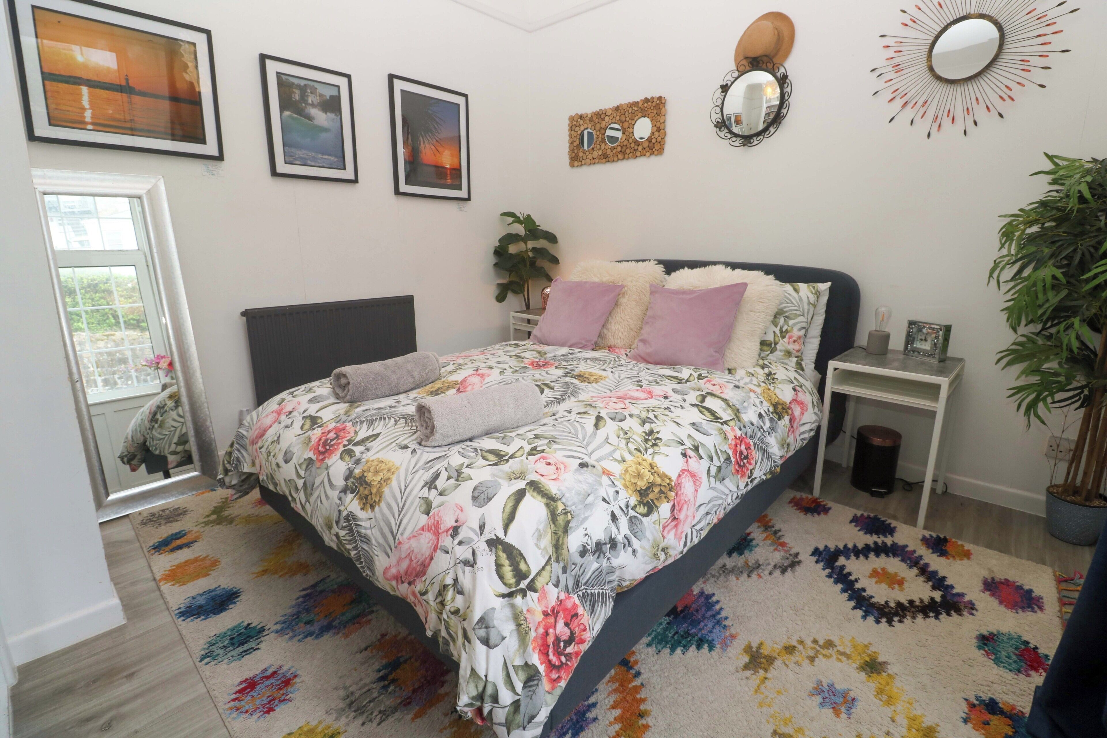 A bedroom with a bed, a bedside table, a mirror, and a potted plant.