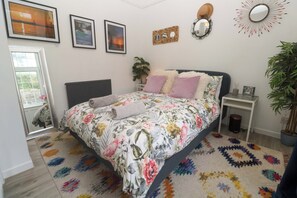 Un dormitorio con cama, mesita de noche, espejo y planta en maceta.