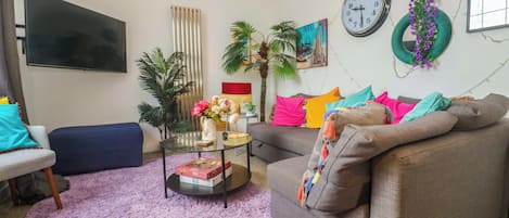 A living room with a sofa, a coffee table, a TV, and a clock on the wall.