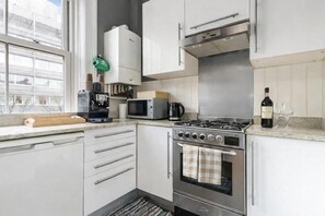 Eine moderne Küche mit Gasherd, Backofen, Mikrowelle, Kaffeemaschine und Blick ins Freie.