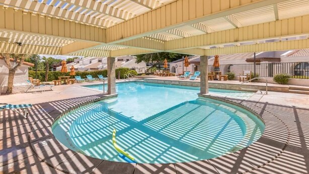 A pool area with a covered section, lounge chairs, and umbrellas. - Cozy 2-bedroom apartment in tranquil St. George with AC and gym Southgate (St. George)