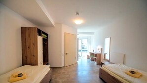 A bedroom with two beds, a wooden wardrobe, a desk with a chair, and a door leading to a balcony. - Accessible Double Room (Schlitz)